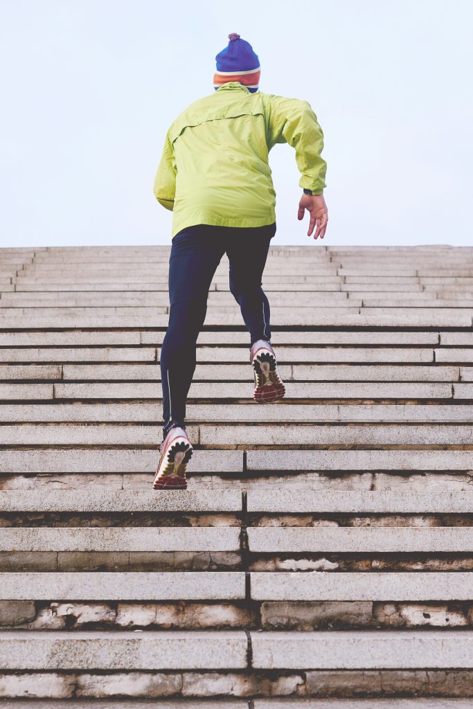Man running up a staircase outdoors, focused on his exercise, showcasing determination and physical fitness.