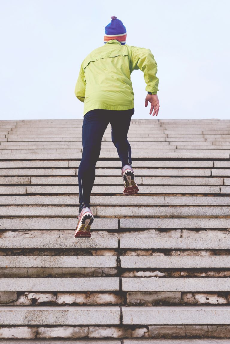 Man running up a staircase outdoors, focused on his exercise, showcasing determination and physical fitness.